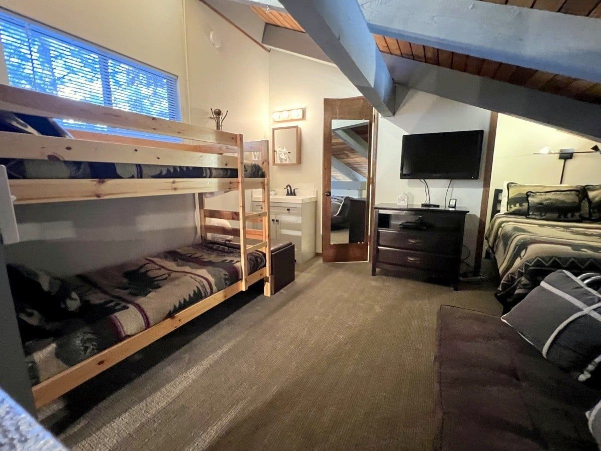 A room with bunk beds, a desk, a television, and a couch.