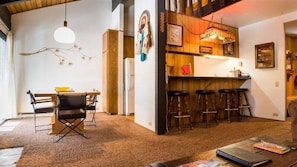 A cozy living room with a wooden dining table, a bar area with stools, and a hanging light fixture. - 2 Bedrooms Standard Condos by RedAwning (Mammoth Lakes)