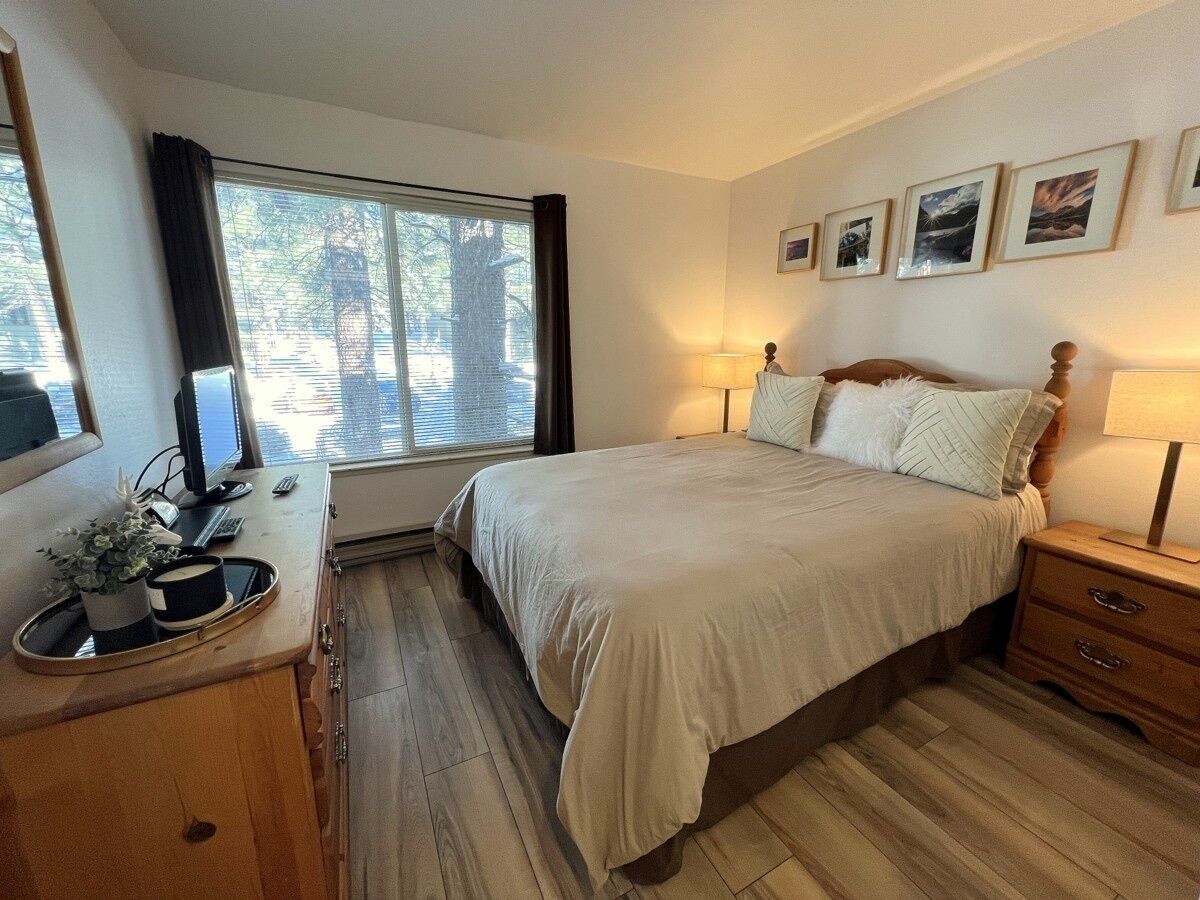 A bedroom with a bed, bedside tables, a desk with a computer, and a window with curtains.