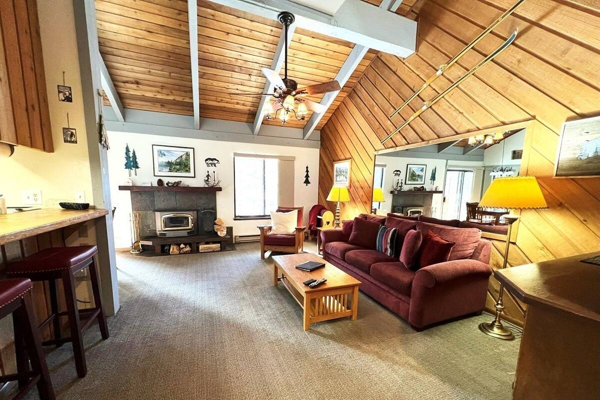 A cozy living room with a fireplace, wooden ceiling, and a dining area with a bar.