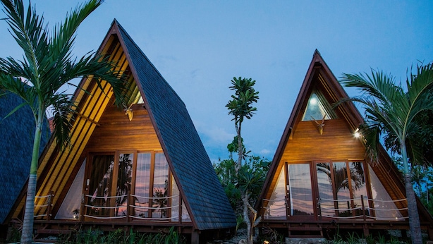 Two wooden triangular bungalows with large windows, surrounded by palm trees. - Batan Sabo Cottage (Penida Island)