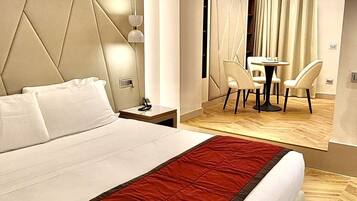 A modern hotel room with a large bed, a red throw blanket, a desk with chairs, and a view through an arched doorway.