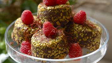 A clear glass plate with several round, nut-topped desserts garnished with raspberries.
