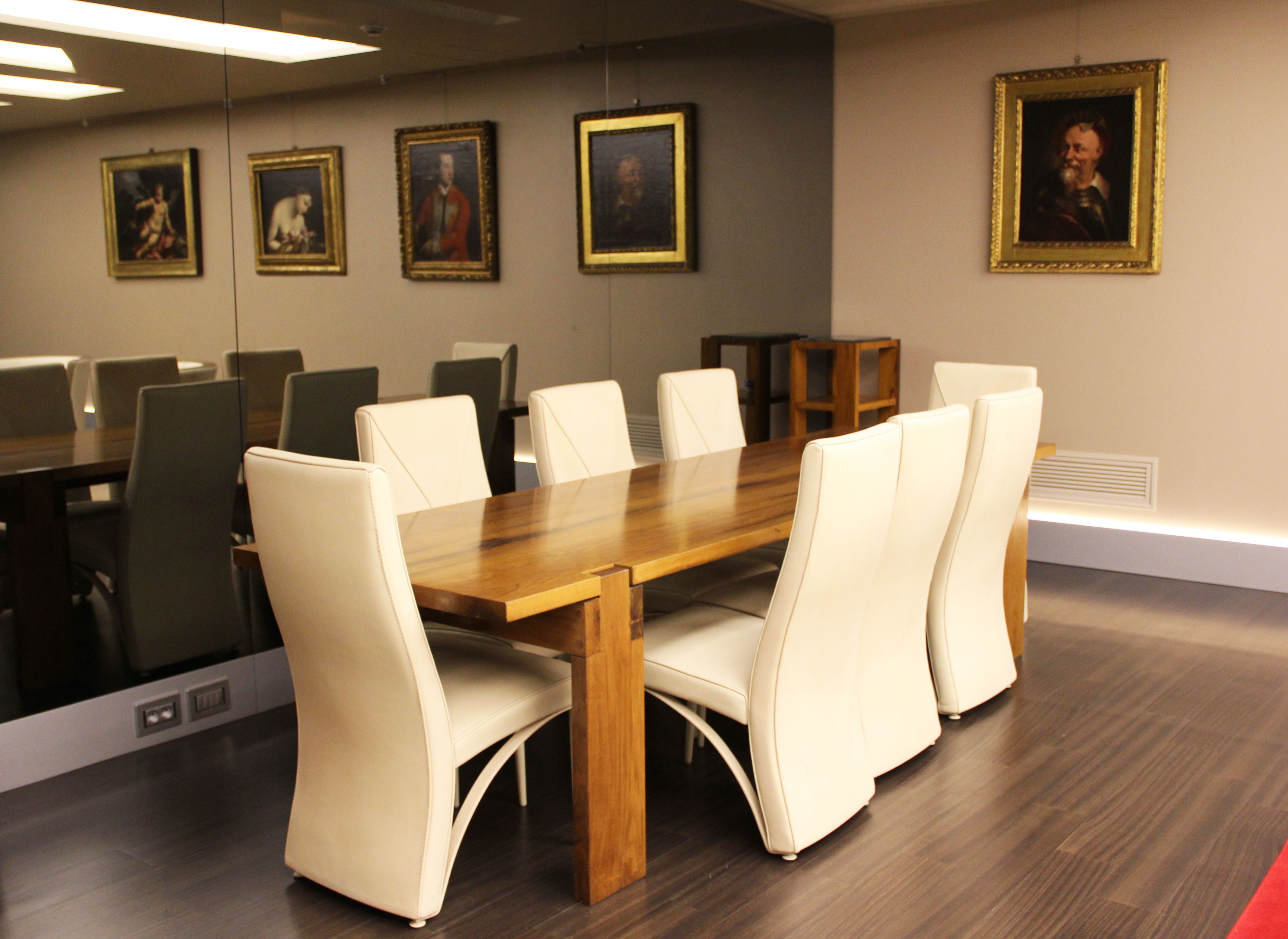 Un salón de conferencias con una mesa de madera y sillas de cuero blanco, obras de arte enmarcadas en las paredes y una mesita auxiliar de madera.