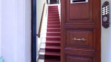 Una puerta de madera con un buzón y una cerradura, que da a una escalera con alfombra roja.