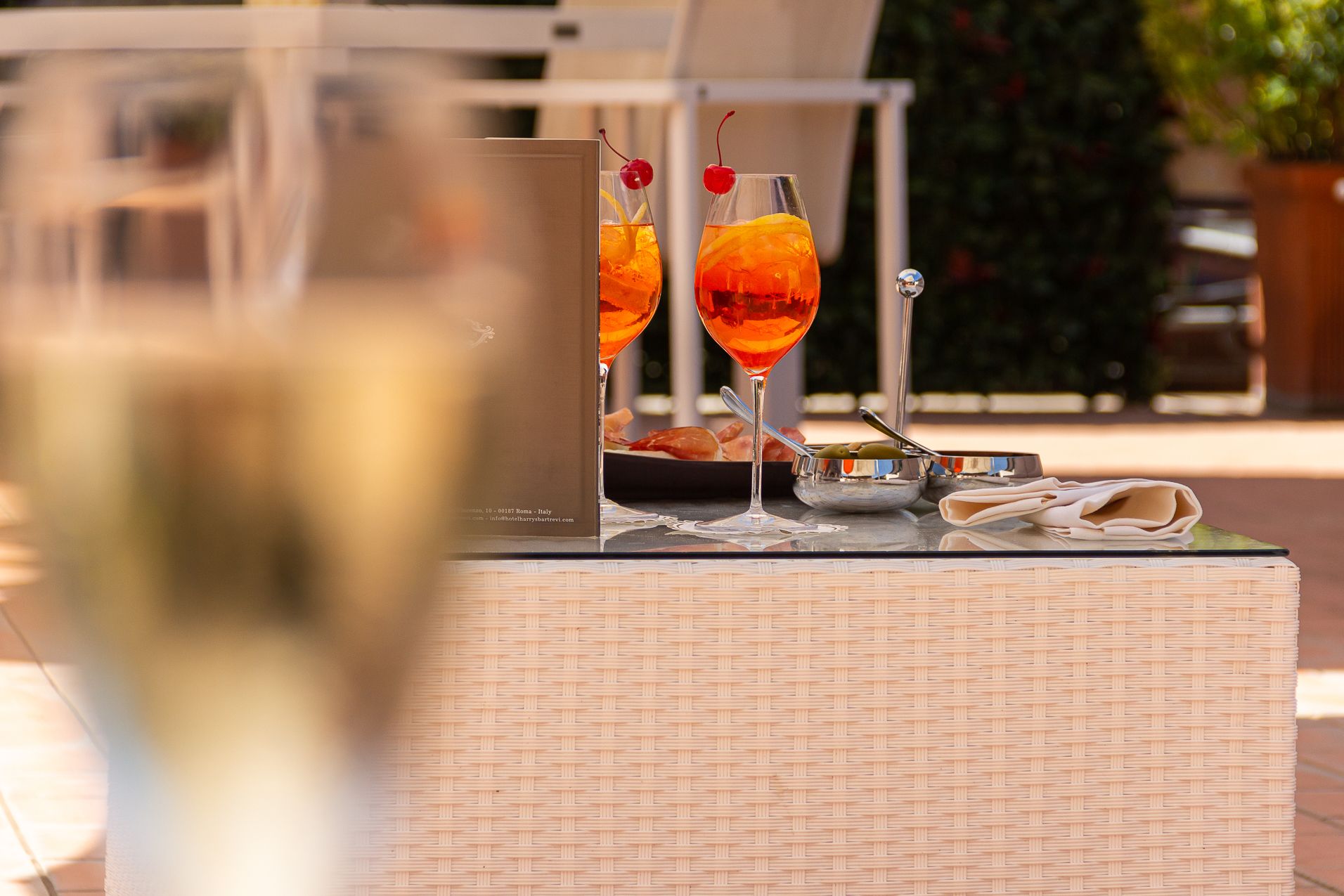 Deux verres de vin rouge sont posés sur une table recouverte d’une nappe en osier, à côté d’une assiette de nourriture et d’une cuillère.