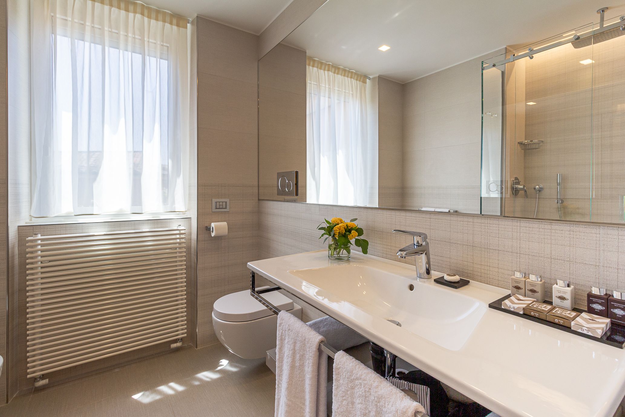 A modern bathroom with a large mirror, a white sink, and a toilet.