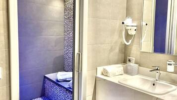 Un baño moderno con cabina de ducha de vidrio, tocador con lavamanos y un espejo grande.