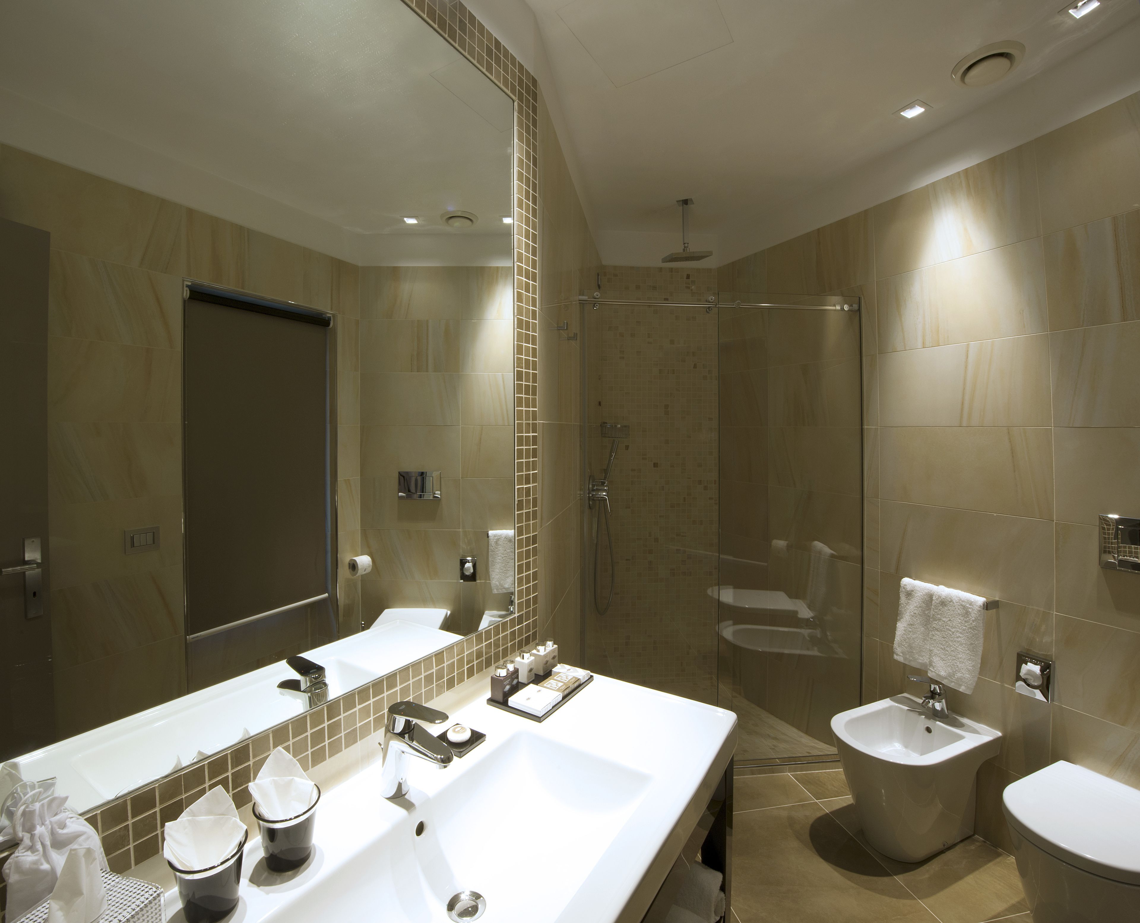 A modern bathroom with a large mirror, two sinks, a shower, and a toilet.
