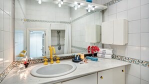 A bathroom with a white sink, yellow faucets, a mirror, and a shower area. - Villetta Caprile (Anacapri)