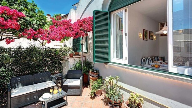 An outdoor patio with wicker furniture, potted plants, and a view of the interior through a glass door. - Villetta Caprile (Anacapri)