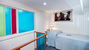 A bedroom with a bed, a nightstand, a lamp, a window with colorful blinds, and a wall painting. - Villetta Caprile (Anacapri)