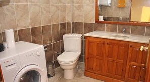 A bathroom with a Bosch washing machine, a toilet, and wooden cabinets.