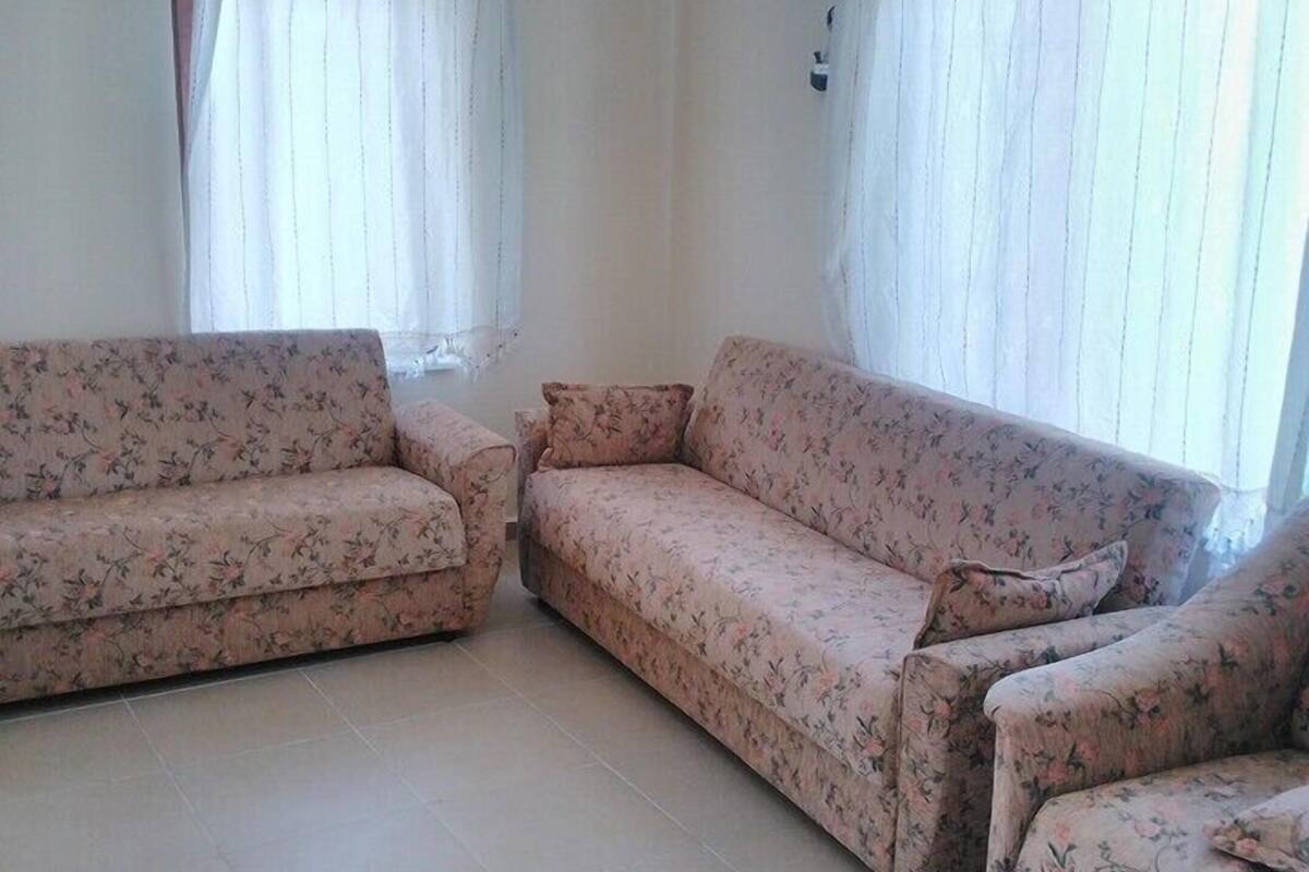 A living room with two floral-patterned sofas, a tiled floor, and a window with white curtains.