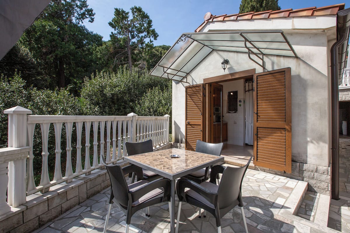 A patio with a table and chairs, a white railing, and a door leading to a covered area.