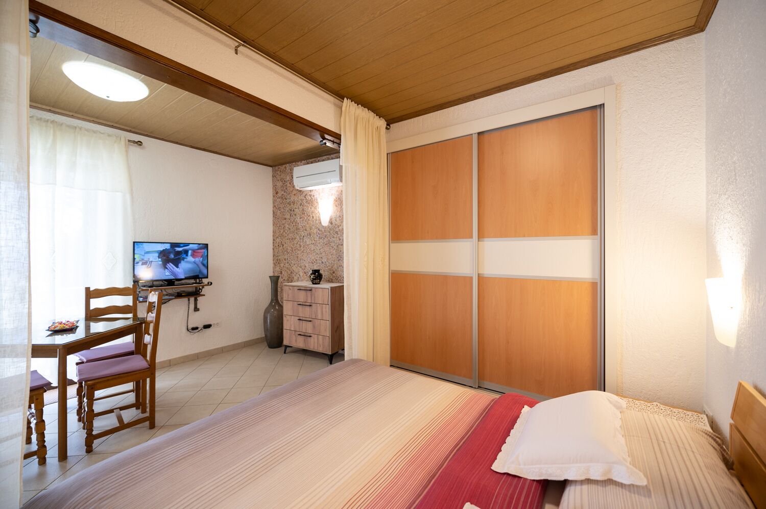 A bedroom with a bed, a TV, a desk, and a wardrobe.