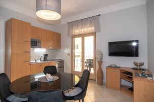 Une cuisine compacte avec des meubles en bois, un four à micro-ondes et une machine à café. On y trouve une table à manger avec des chaises, ainsi qu’un téléviseur fixé au mur.