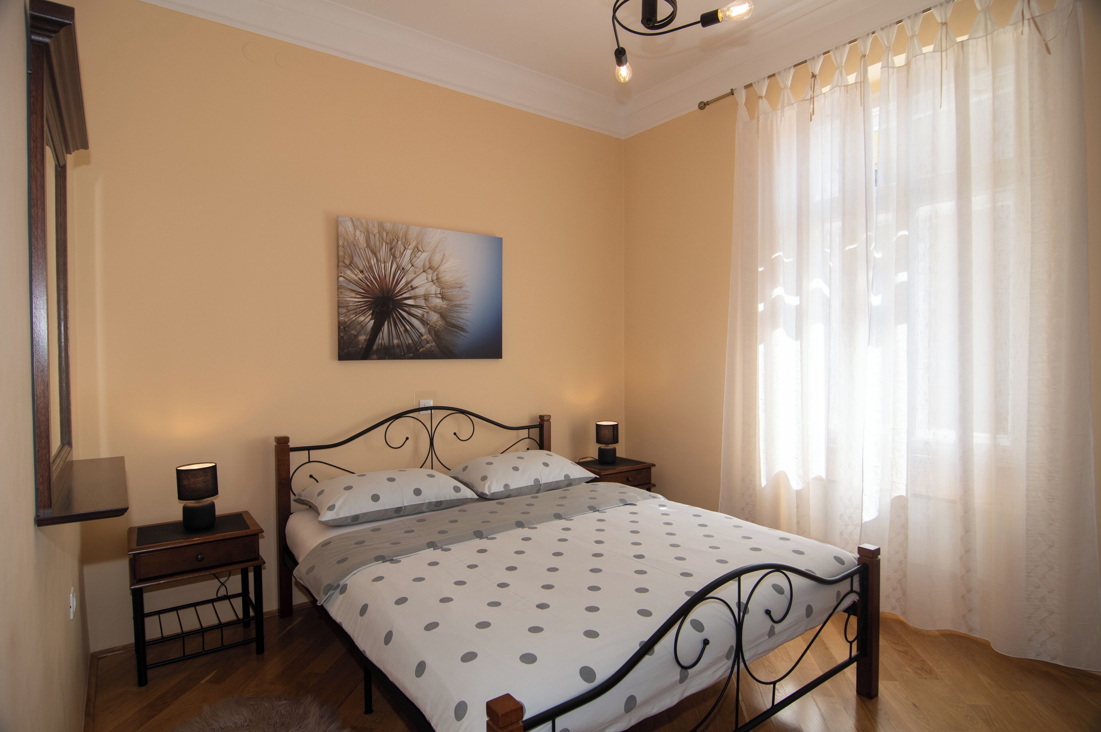 A bedroom with a bed, nightstands, a lamp, a painting, and a window with curtains.