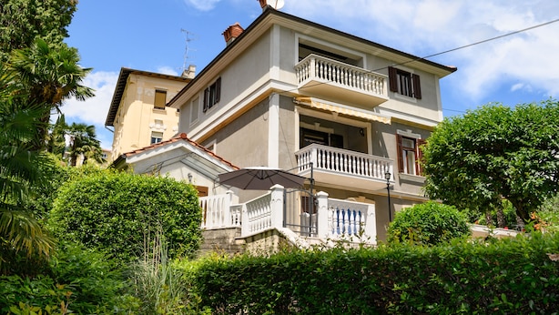 A two-story building with a balcony, surrounded by lush greenery.