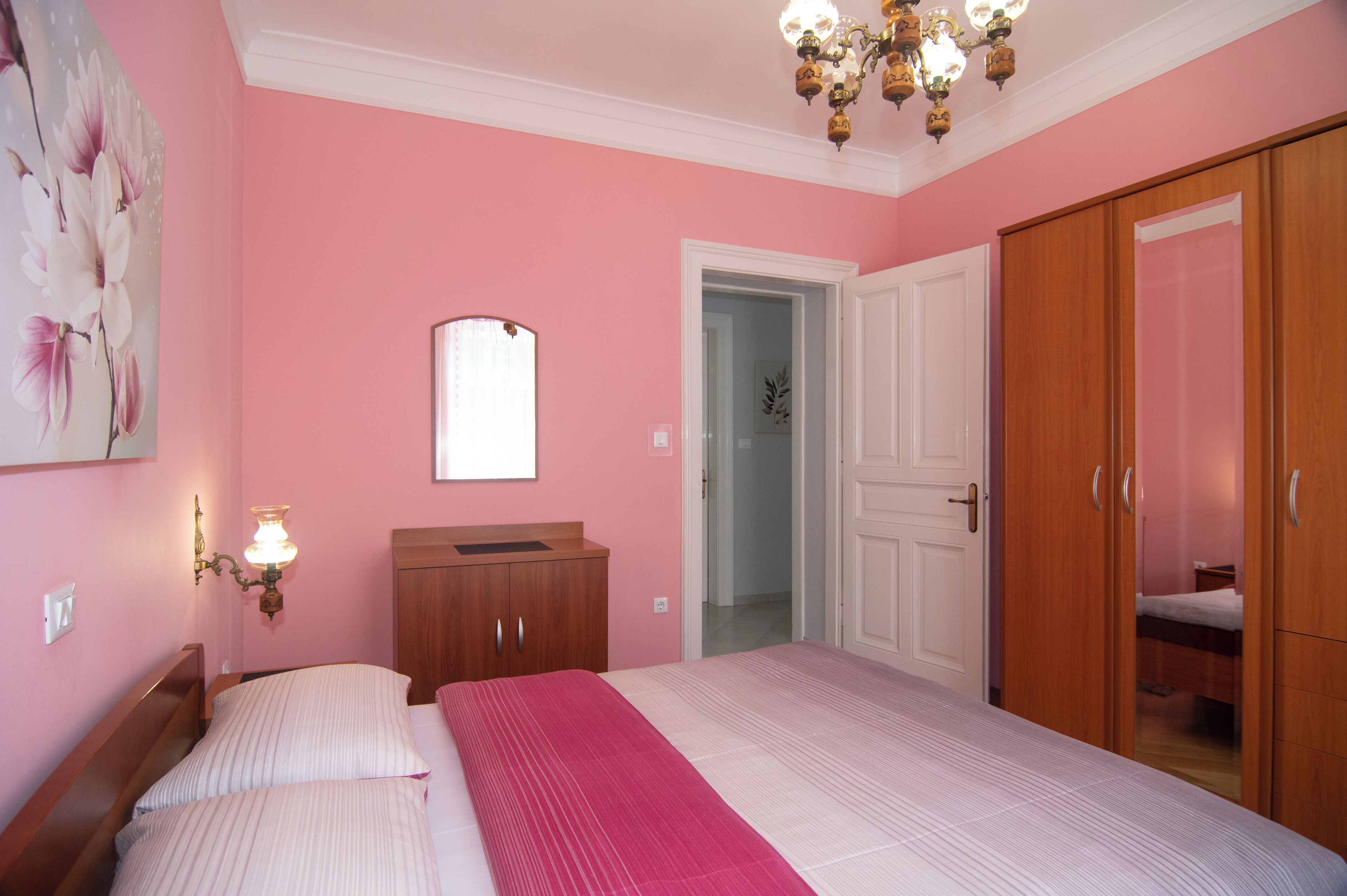 A bedroom with a large bed, a wooden wardrobe, a mirror, and a chandelier.