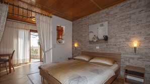 A bedroom with a wooden bed, a desk, and a chair. There is a window with curtains, a wall-mounted shelf with jars, and two wall sconces.