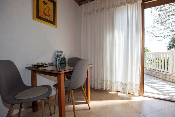 A dining area with a table and two chairs, a framed picture on the wall, and a view of a white fence and greenery outside. - Villa Salona (Opatija)