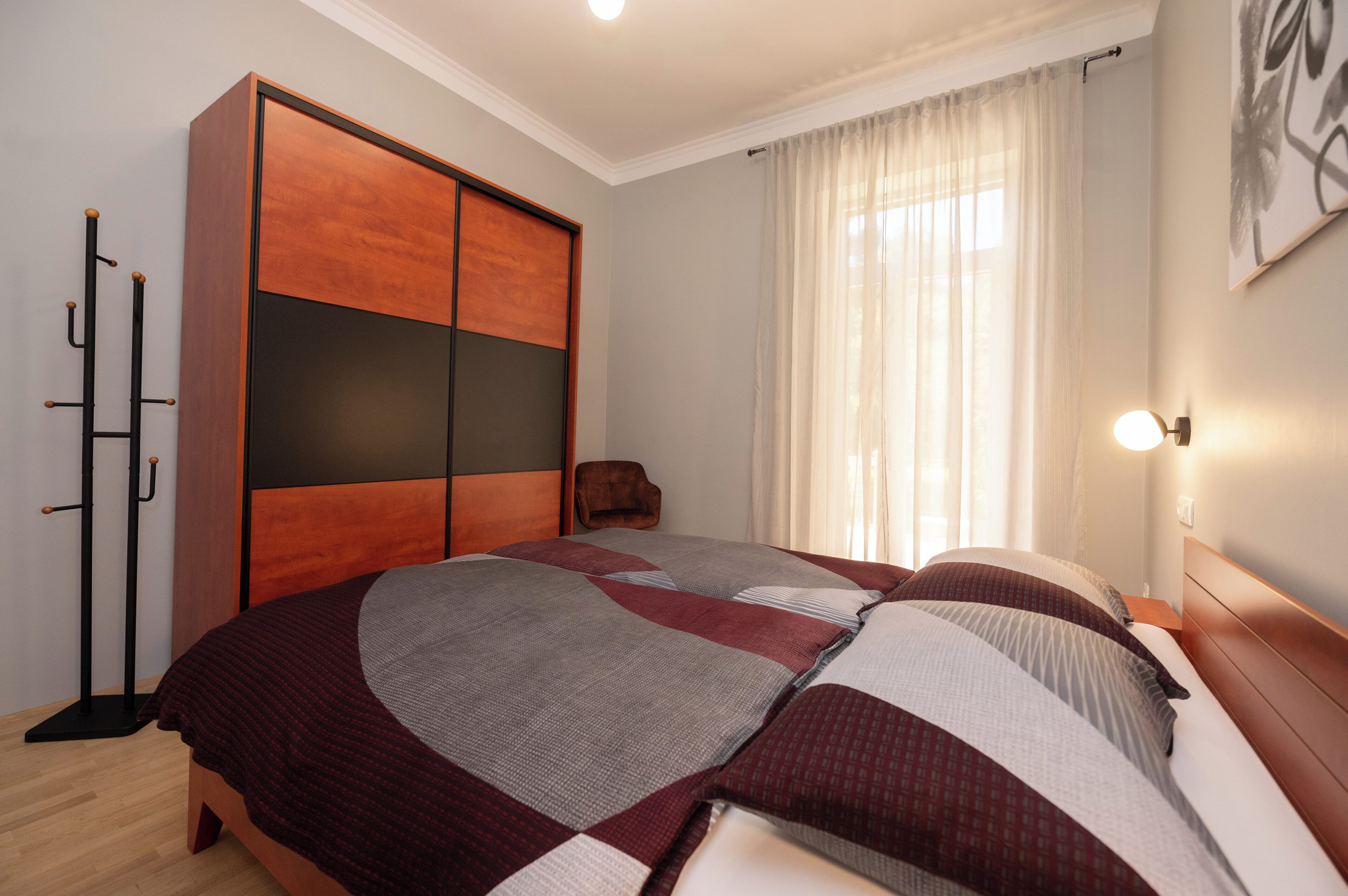 A bedroom with a large bed, a wardrobe, a chair, and a window with curtains.