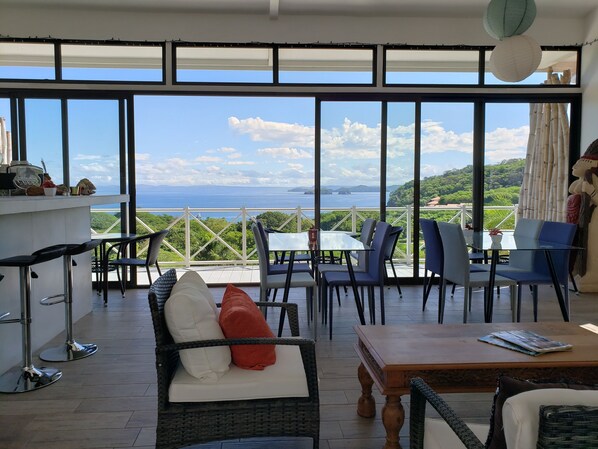 A terrace with wicker furniture, a wooden table, and a view of the sea.
