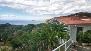 Une vue sur la côte, avec un bâtiment doté d’un toit recouvert de tuiles rouges, entouré d’une végétation luxuriante et sous un ciel dégagé.