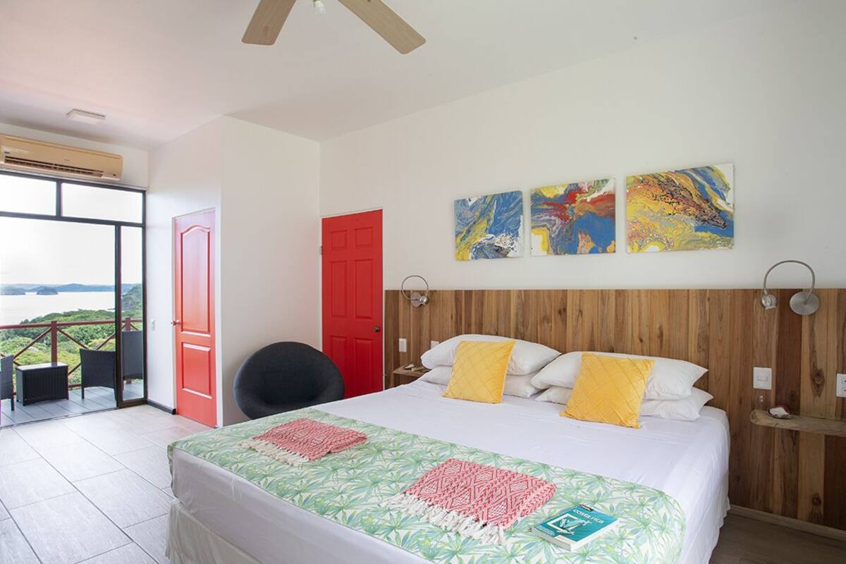 Habitació d'hotel amb llit, un balcó i vistes, una porta vermella i obra d'art abstracta a la paret.