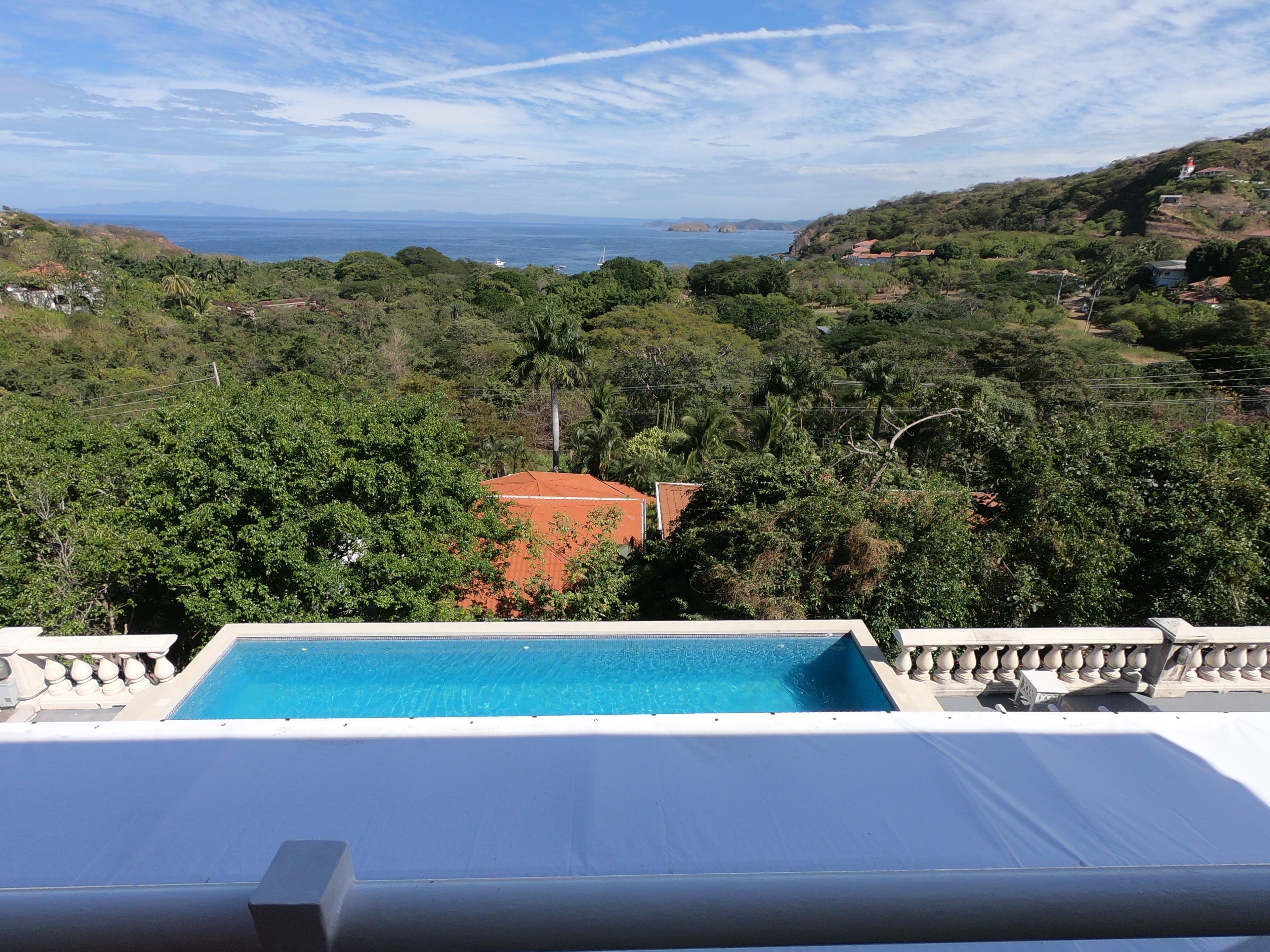 A pool with a view of a coastal landscape, including trees and a distant view of the sea.