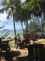 An outdoor seating area with tables and chairs, overlooking a beach and the sea.