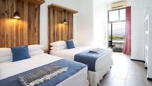 Une chambre d’hôtel avec deux lits, des têtes de lit en bois et une vue sur la mer, visible à travers une grande fenêtre.