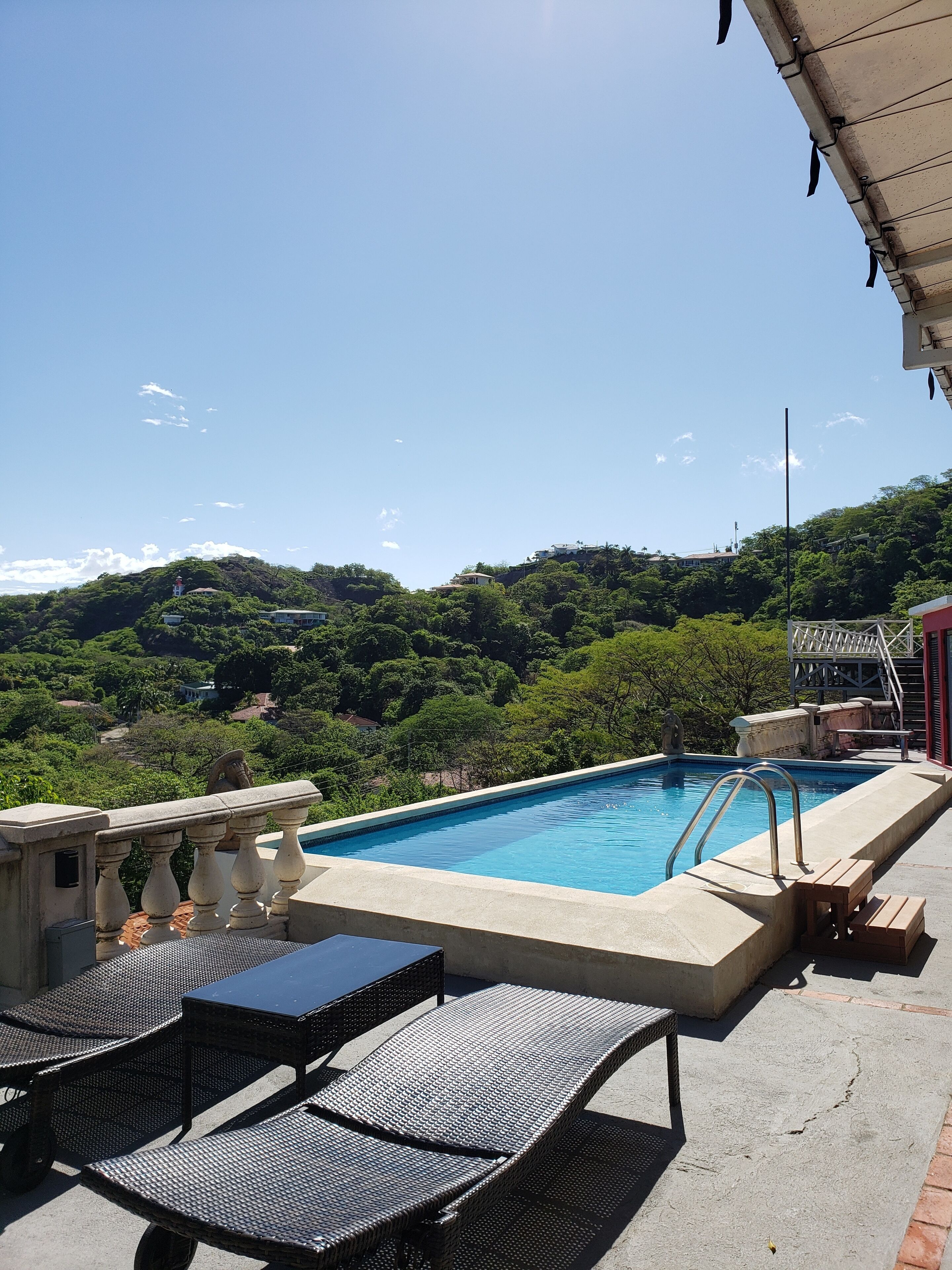 A pool area with a view of a hillside, outdoor seating, and a staircase leading to a terrace.