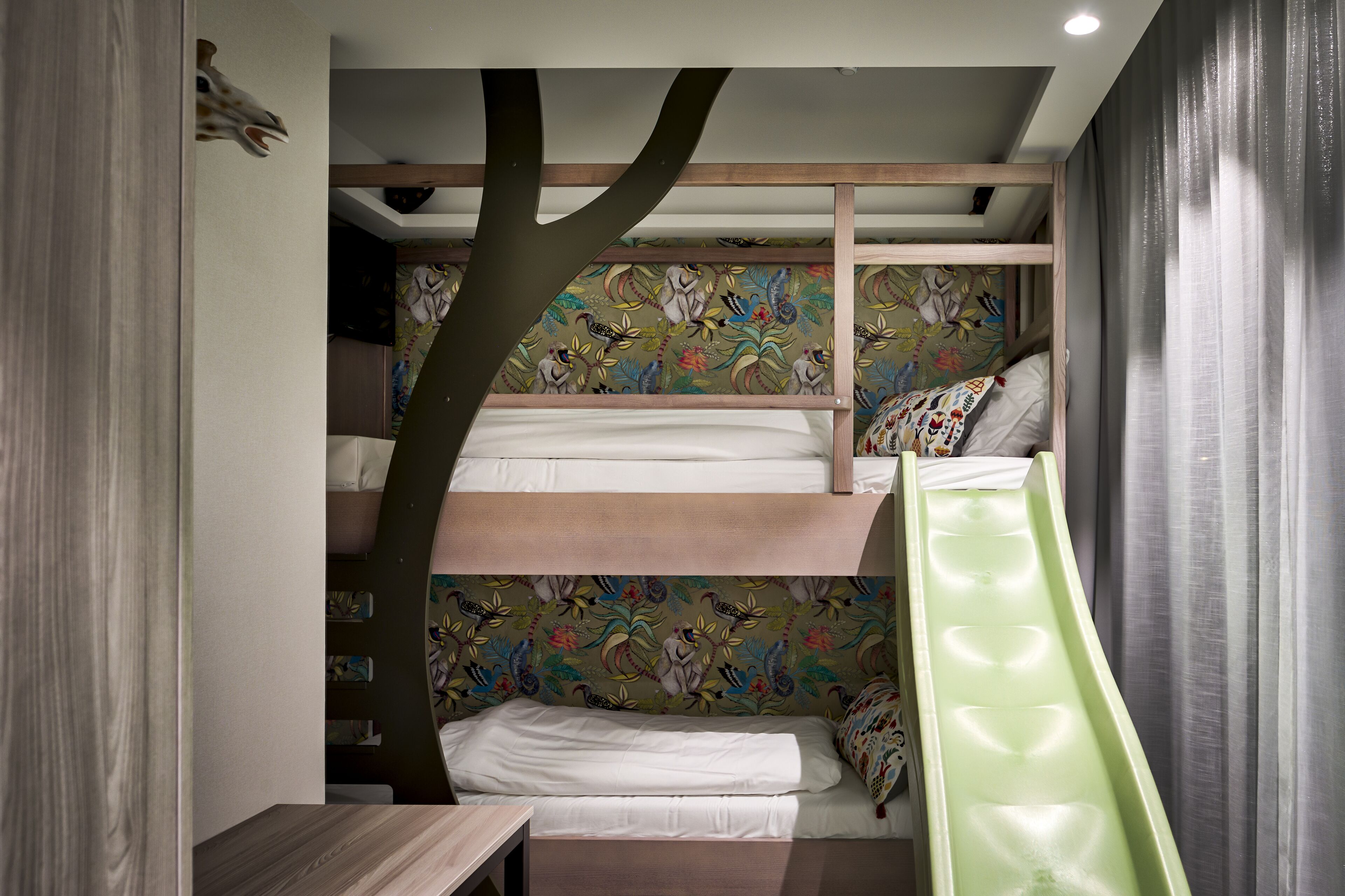 Dormitorio con literas que simula la forma de un árbol, un tobogán verde y pared con diseño.