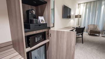 A hotel room with a kitchenette, a TV, a desk, a chair, and a sofa.