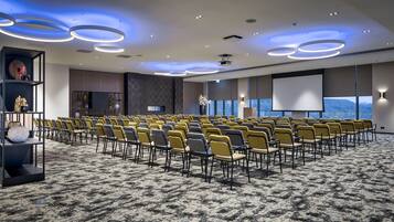 A conference room with rows of chairs, a projector screen, and a large window with a view.