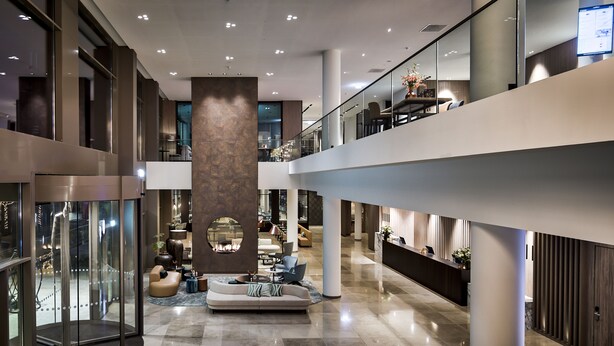 A spacious lobby with a central seating area, a reception desk, and a glass elevator. - Van der Valk Hotel Tilburg (Tilburg)