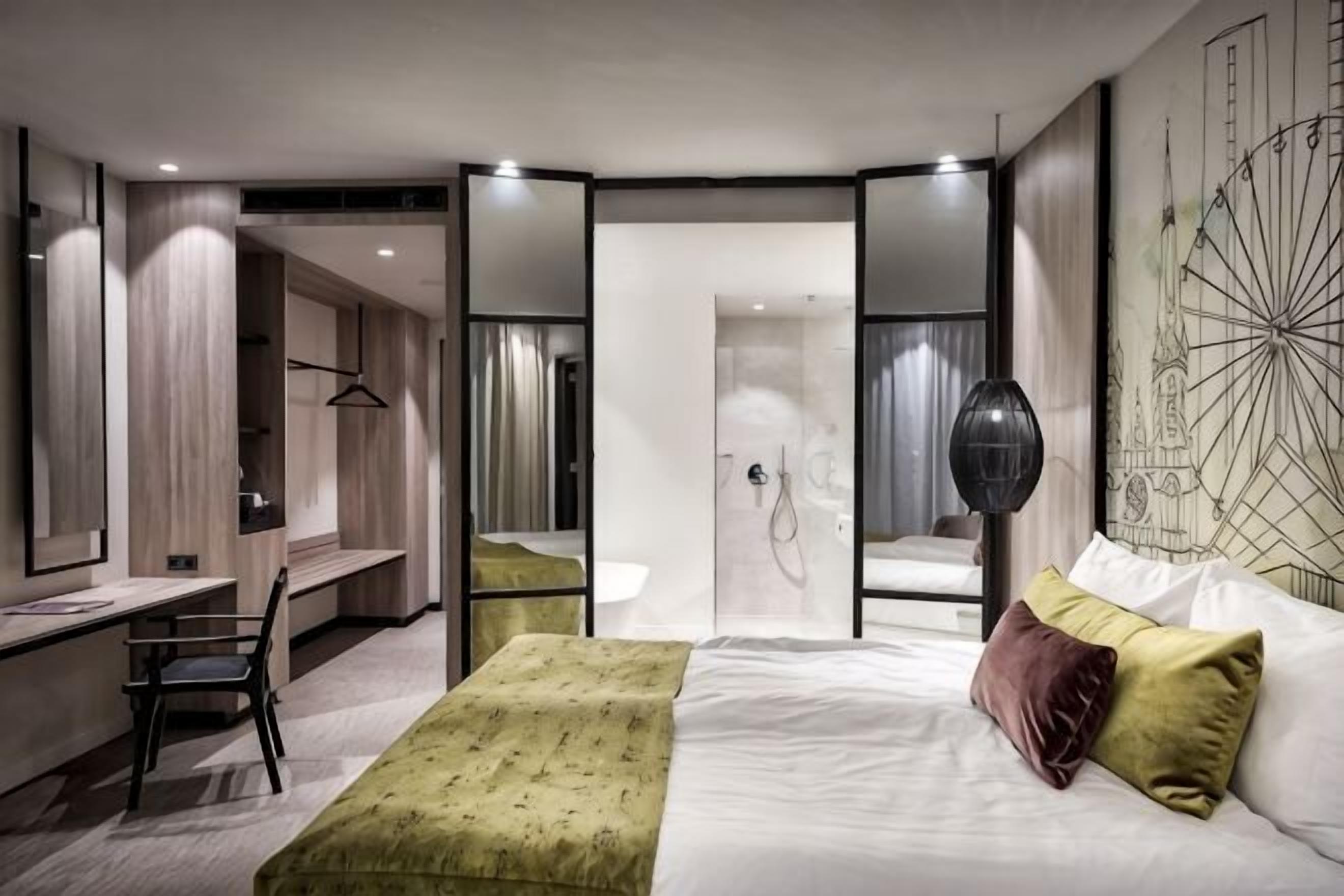 Ett modernt hotellrum med en säng, ett skrivbord, en stol, en spegel och en garderob.