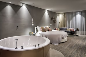 A modern bedroom with a large bathtub, a bed with multiple pillows, and a sofa.