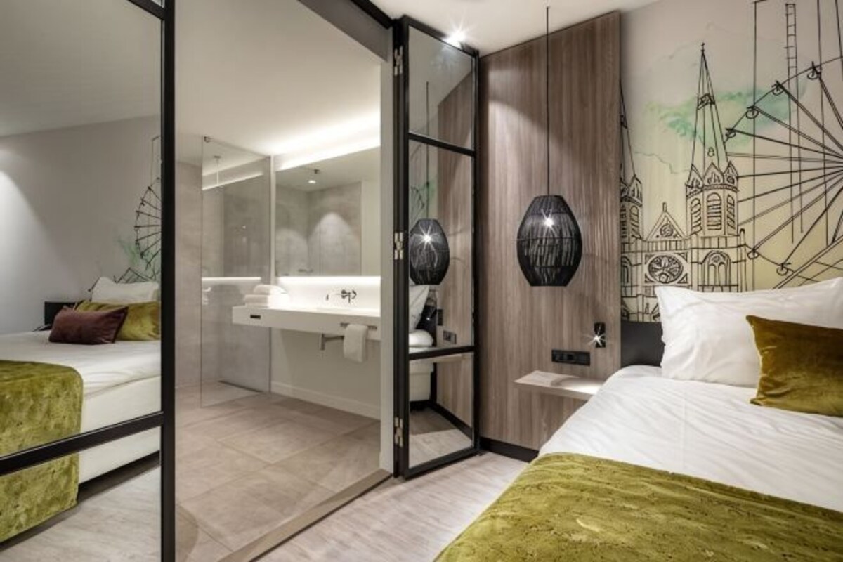 Una habitación de hotel moderna con cama, espejo, baño y una pared con diseño de paisaje urbano.