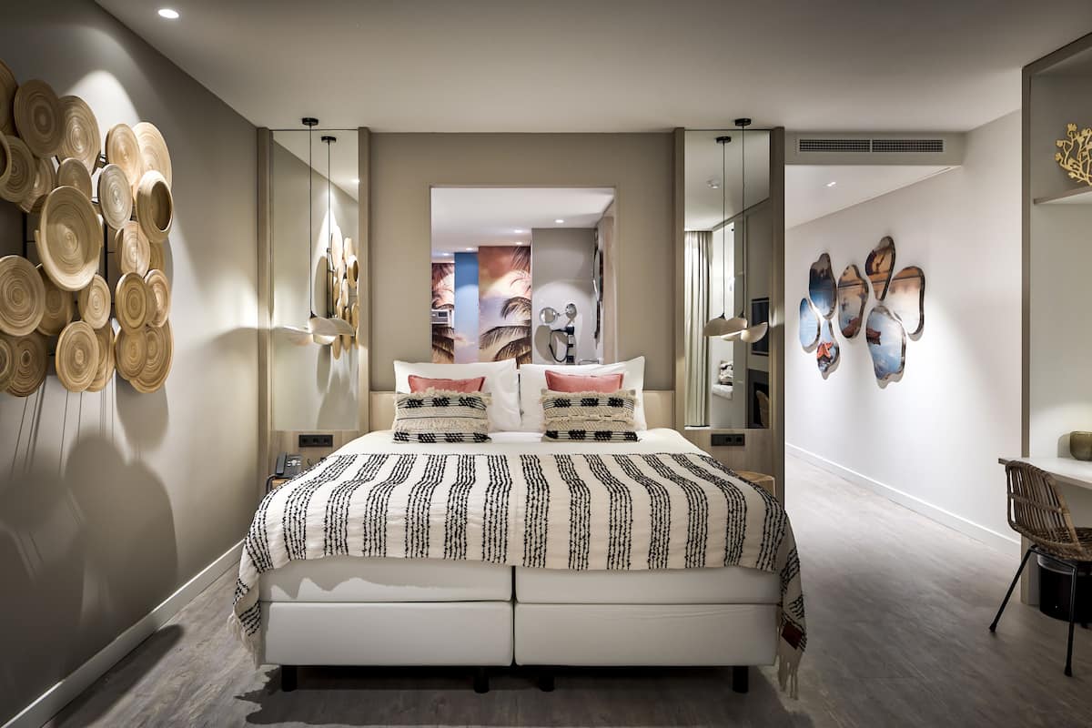A modern bedroom with a large bed, a wall-mounted mirror, and a decorative wall piece.