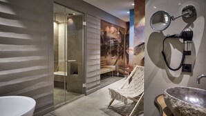 A modern bathroom with a large white sink, a glass shower enclosure, and a seating area with a macrame chair. - Van der Valk Hotel Tilburg (Tilburg)