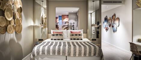 A modern bedroom with a large bed, a bedside table, a chair, and wall art.