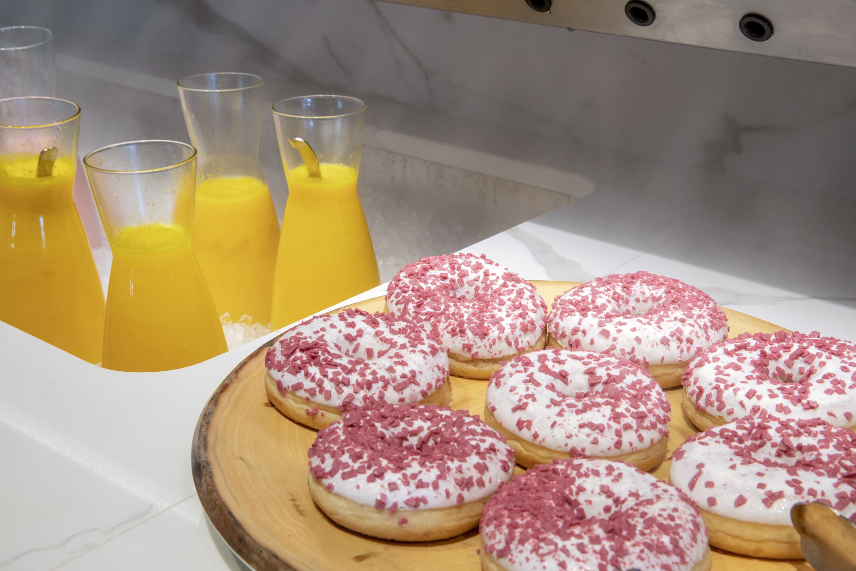 A breakfast setting with a tray of pink and white frosted donuts and a pitcher of orange juice.