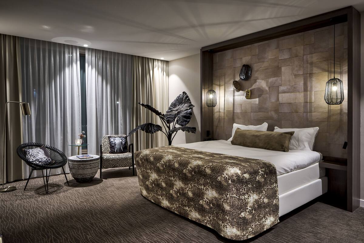 A modern bedroom with a large bed, a side table, a chair, and a decorative wall panel.