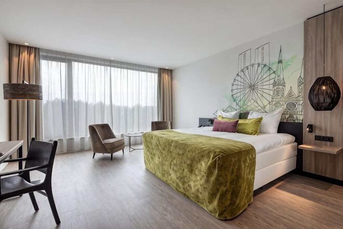 Habitación de hotel moderna con una cama grande, un escritorio, una silla y vistas a la ciudad a través de amplios ventanales.