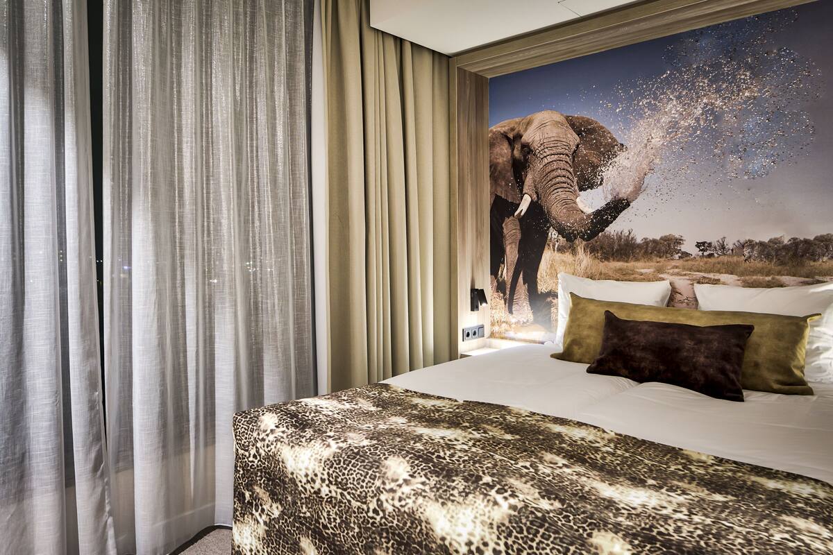 A hotel room with a large bed, a leopard print bedspread, and a poster of an elephant.