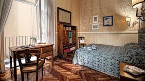 Une pièce comprenant un bureau en bois, une bibliothèque, un lit recouvert d’une couvre-lit à motifs et un mur orné de tableaux encadrés.