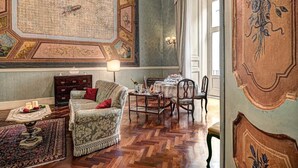 Une pièce avec un tapis à motifs, un canapé avec des coussins rouges, une table à manger entourée de chaises et un lustre.